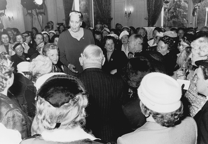 Käte Ahlmann bei einer Ansprache, auf einem Stuhl stehend. Vor ihr Bundeskanzler Ludwig Erhard.